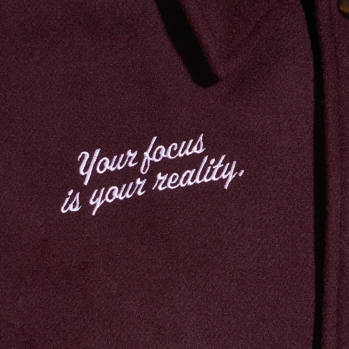 Close-up of a dark burgundy fabric with white embroidered script reading 'Your Focus Is Your Reality.'