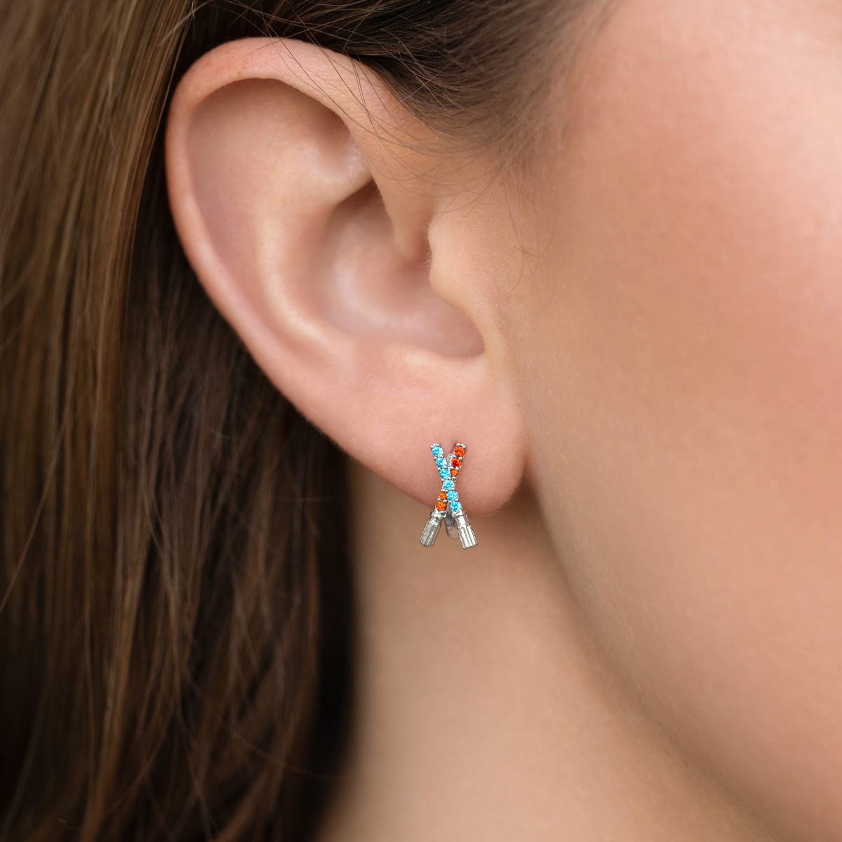 Pair of silver-tone stud earrings featuring crossed lightsaber-inspired motifs accented with alternating blue and red crystals, photographed on a model's ear.
