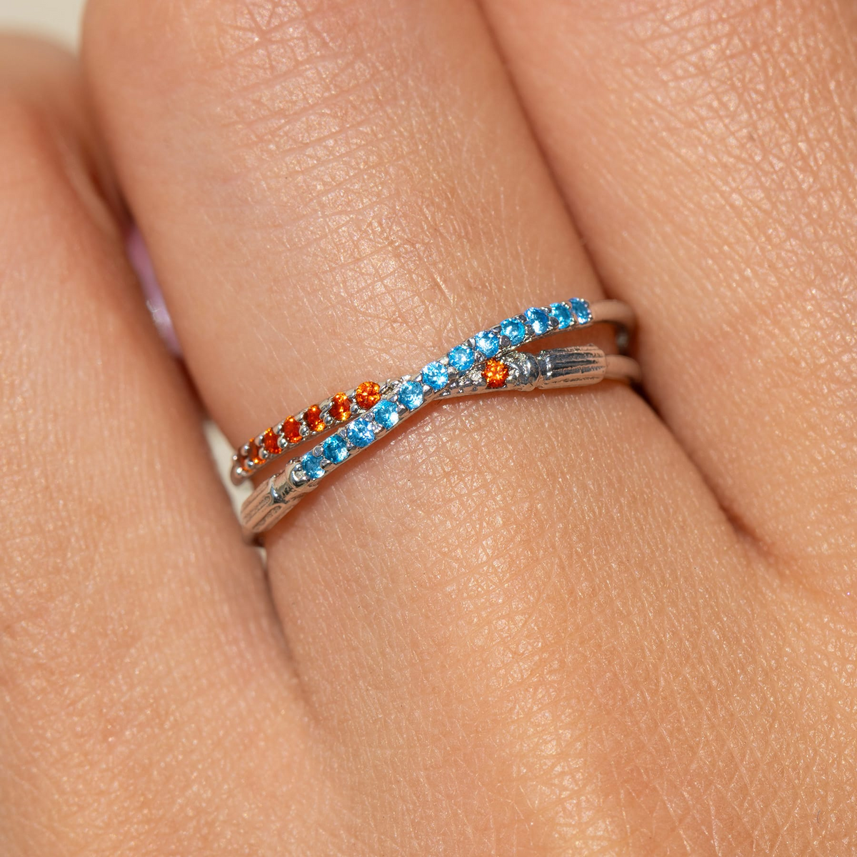 Silver-tone crossover ring featuring two lightsaber-inspired bands accented with alternating blue and red crystals, displayed around a model's finger.