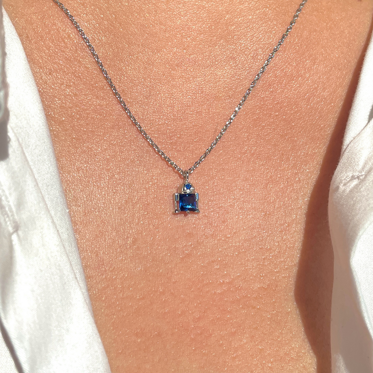 Silver-tone R2-D2 necklace featuring a stylized droid-shaped pendant accented with blue crystals and clear pavé details, displayed around a model's neck.