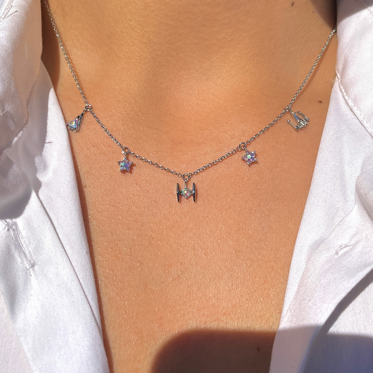 Silver-tone Starfighter Charm Necklace featuring a delicate chain adorned with iridescent star and crystal charms, a central starfighter-inspired pendant, and additional celestial accents, displayed around a model's neck.