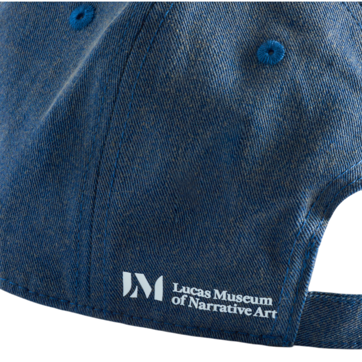 Side close-up of a washed cotton denim dad hat featuring a white Lucas Museum of Narrative Art logo and text.