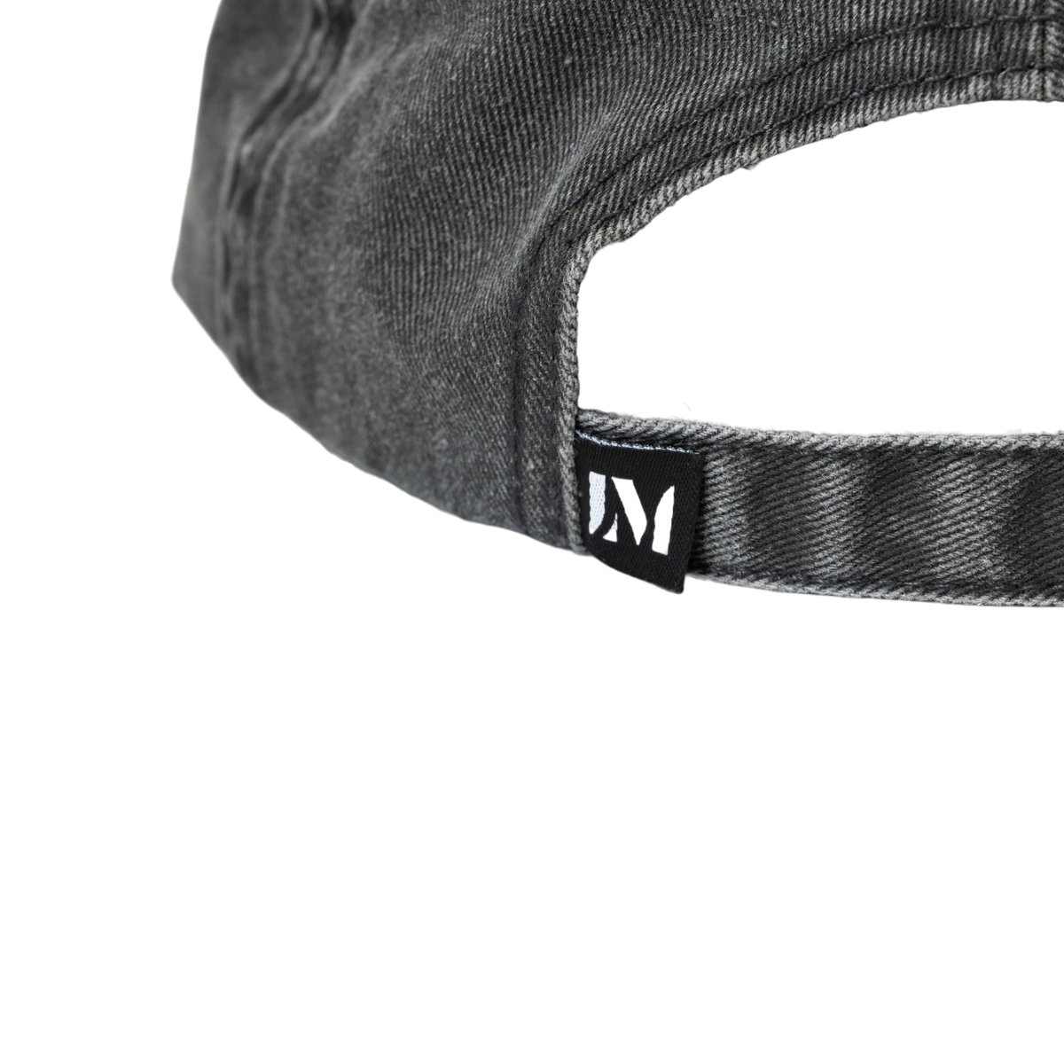 Close-up of the back strap of a washed black denim baseball cap, featuring a black fabric tag with a white stylized Lucas Museum of Narrative Art logo.