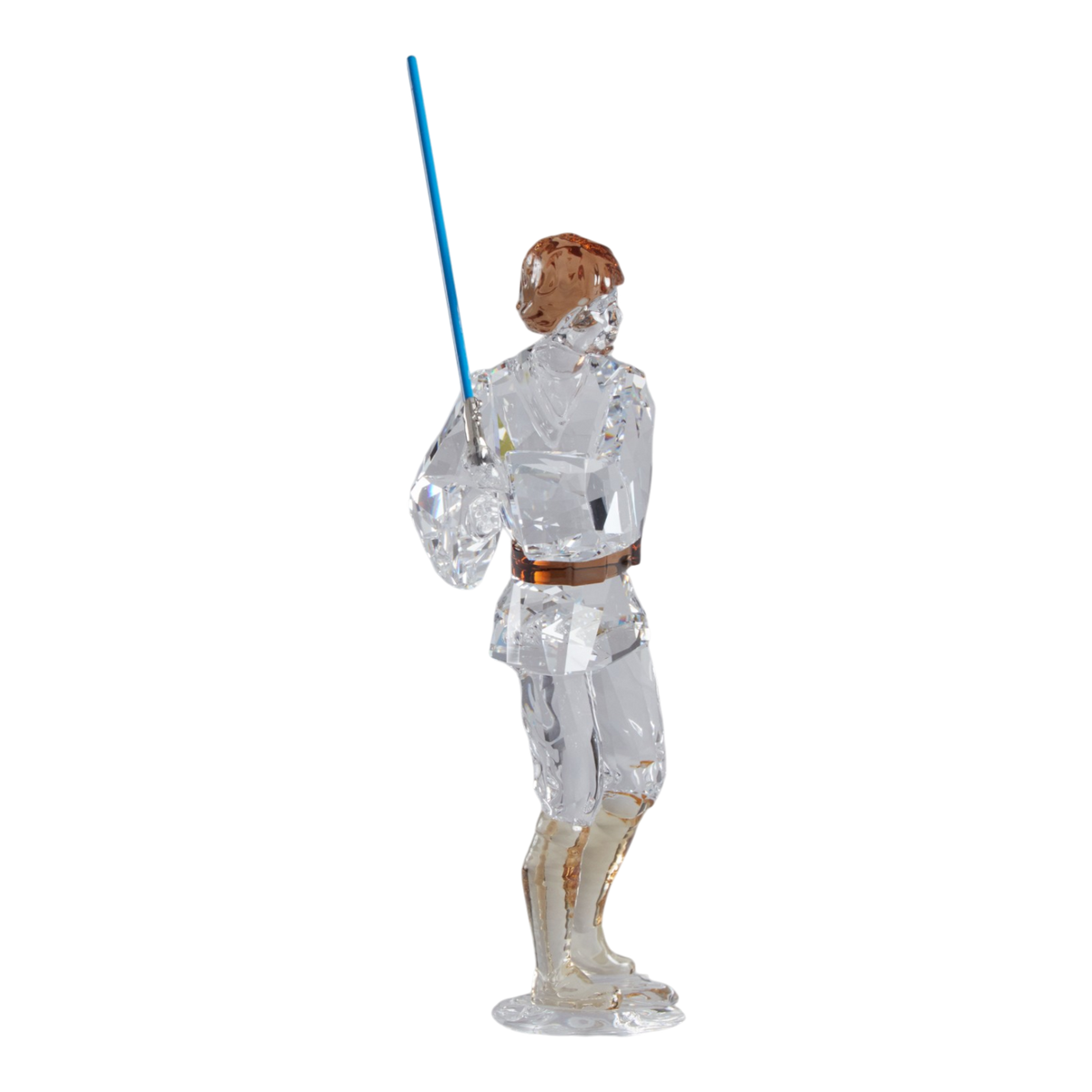 A clear faceted Swarovski crystal figurine of Luke Skywalker holding a blue sword, standing on a transparent base against a plain white background.