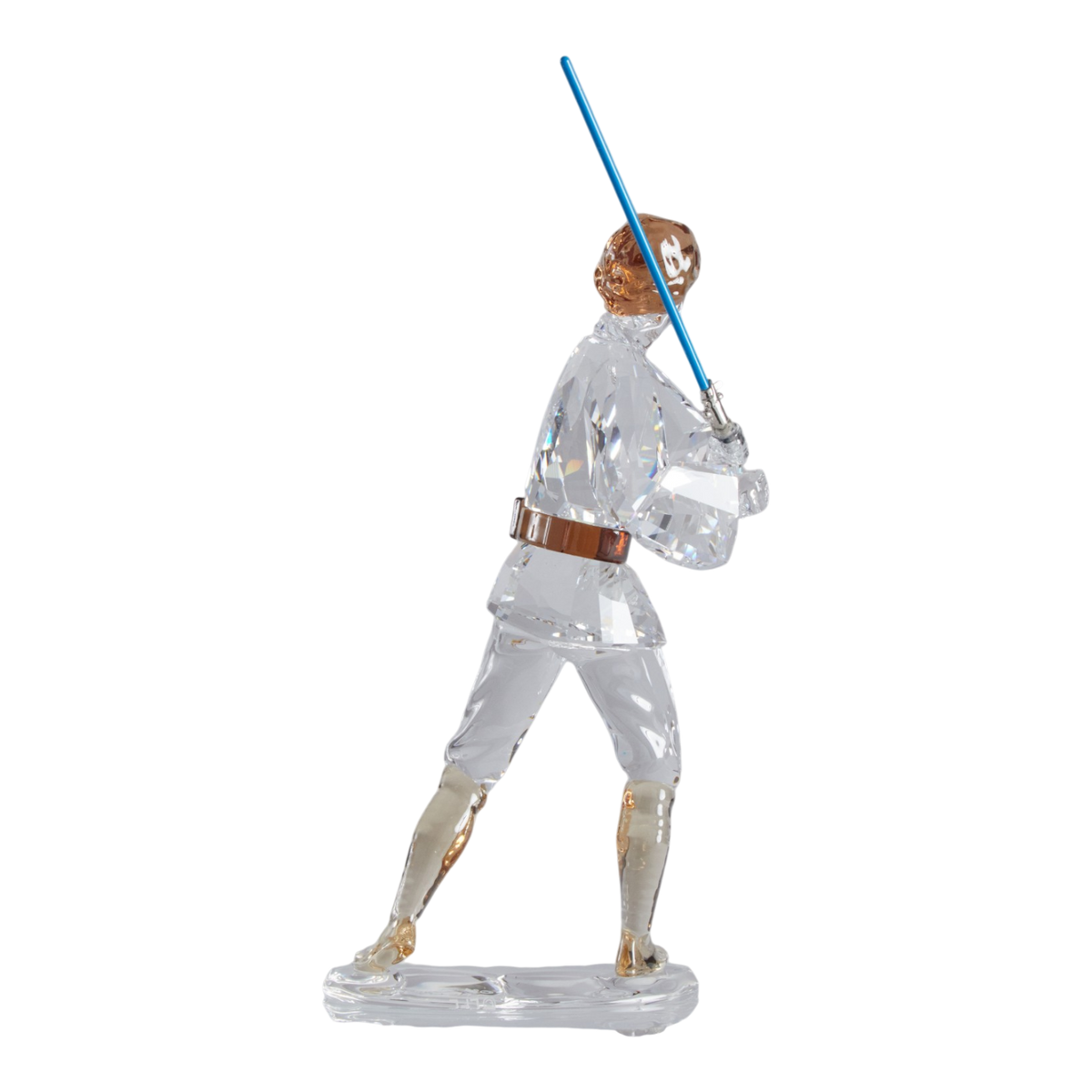 A clear faceted Swarovski crystal figurine of Luke Skywalker holding a blue sword, standing on a transparent base against a plain white background.