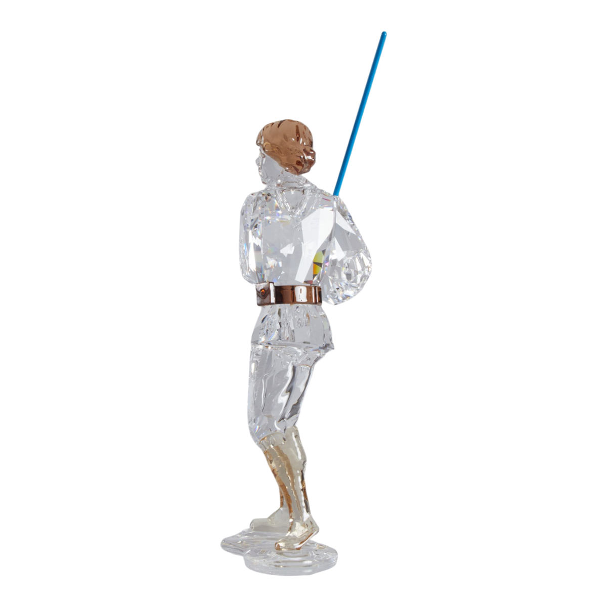 A clear faceted Swarovski crystal figurine of Luke Skywalker holding a blue sword, standing on a transparent base against a plain white background.