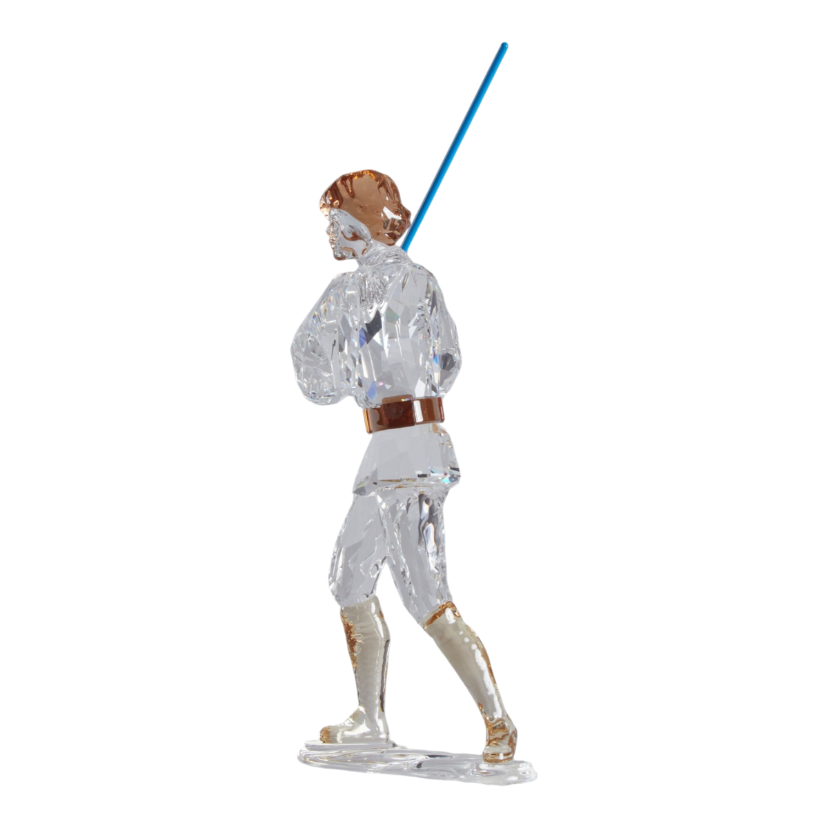 A clear faceted Swarovski crystal figurine of Luke Skywalker holding a blue sword, standing on a transparent base against a plain white background.