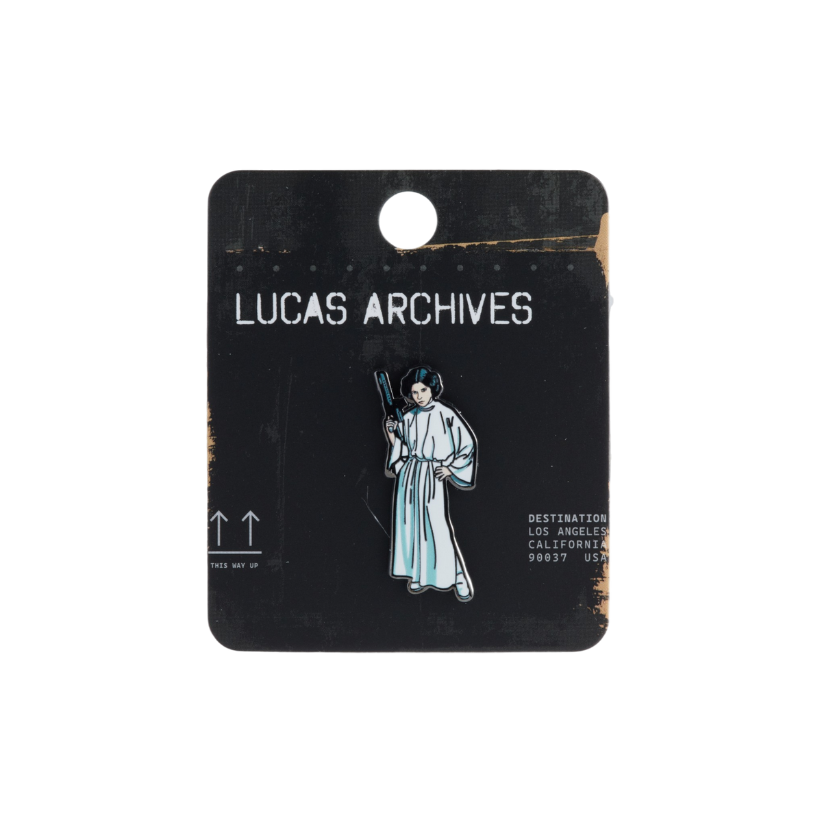 A Lucas Archives enamel pin of Princess Leia in a white robe holding a gun, mounted on a black display card with white text.