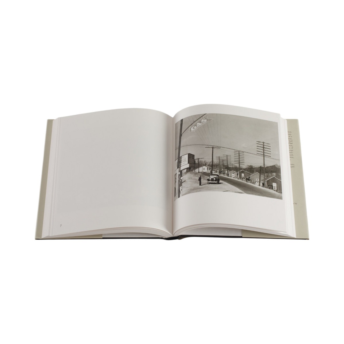An open hardcover book on a plain white background, showing an interior spread with blank white pages on the left and a black-and-white street photograph printed on the right page.