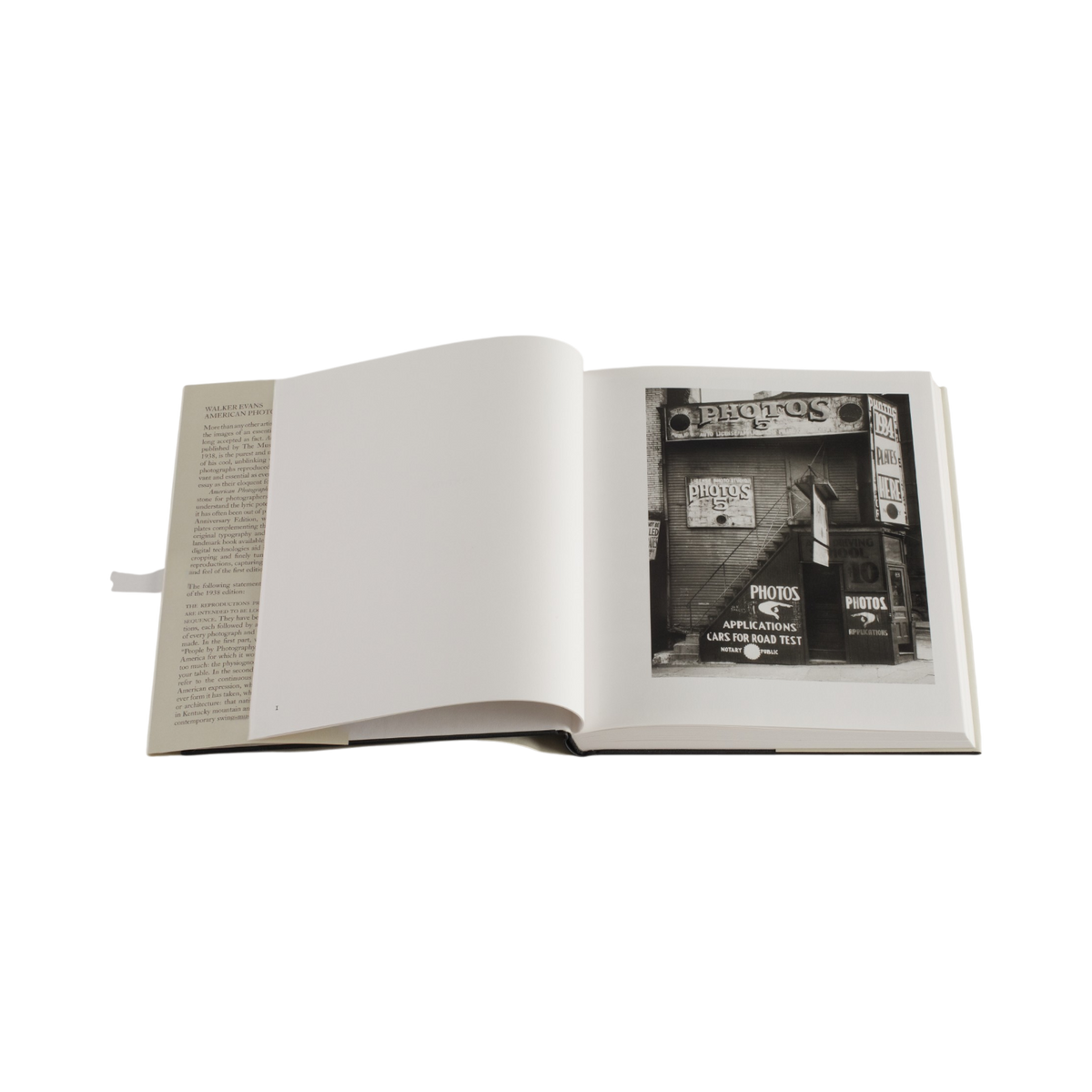 An open hardcover book on a plain white background, showing a black-and-white street photograph printed on the right page and text on the left page.