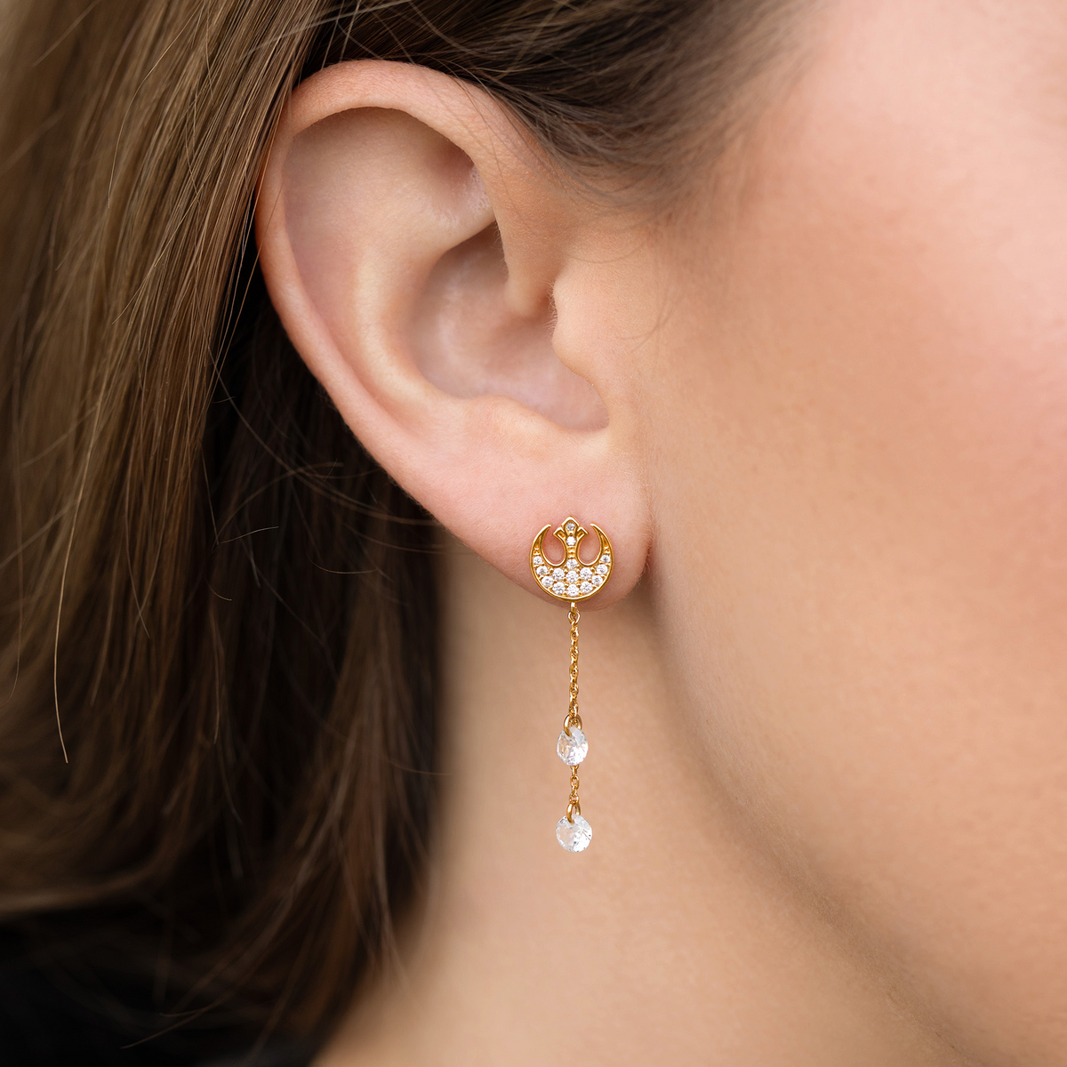 Gold-tone Rebel Alliance insignia dangle earring featuring clear crystal pavé accents and suspended round crystal charms, photographed on a model's ear.