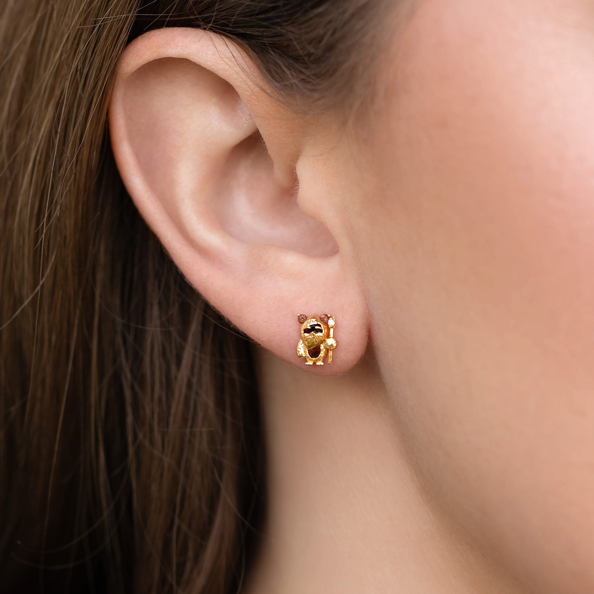 Gold-tone Ewok stud earring featuring a sculpted character design with brown crystal accents and staff details, photographed on a model's ear.