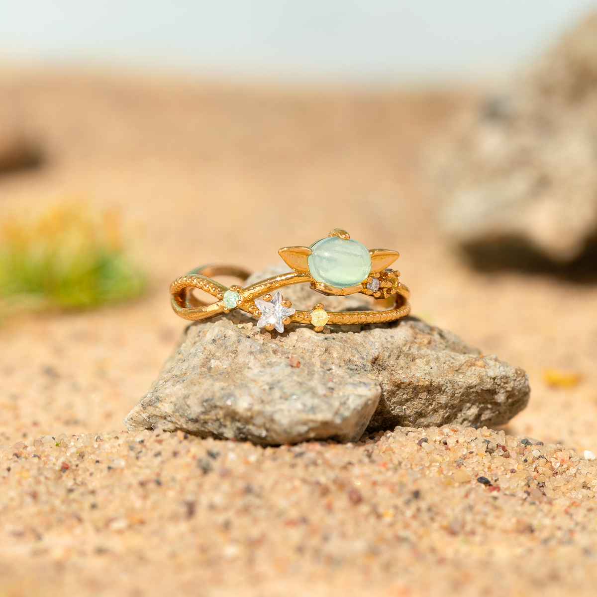 Gold-tone adjustable Grogu Galaxy ring featuring a luminous oval centerpiece surrounded by planetary and star-inspired details, accented with multicolored crystals and metallic star motifs, displayed on a rock in a natural setting.