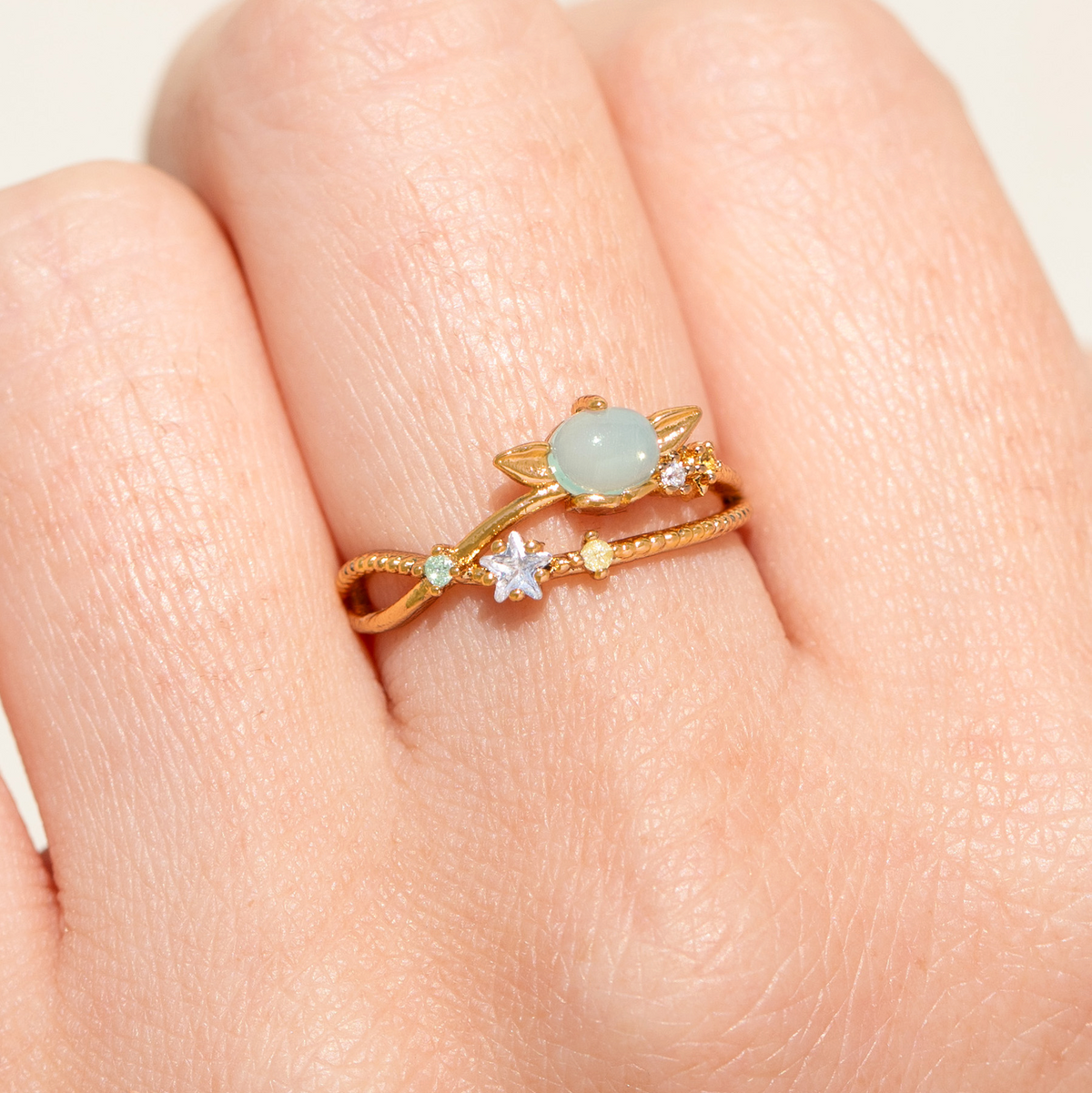 Gold-tone adjustable Grogu Galaxy ring featuring a luminous oval centerpiece surrounded by planetary and star-inspired details, accented with multicolored crystals and metallic star motifs, shown on a model's hand.