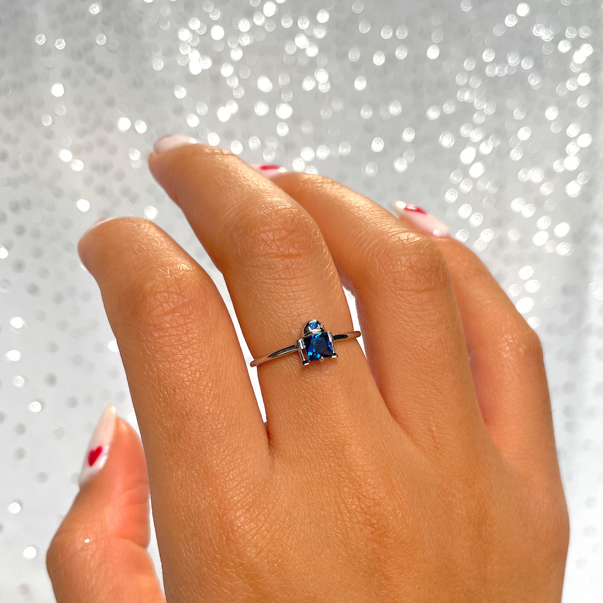 Silver-tone R2-D2 ring featuring a stylized droid-inspired design with a blue crystal centerpiece and blue accent stone, displayed around a model's finger.