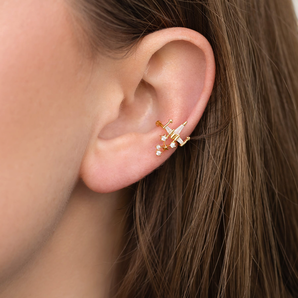 Gold-tone X-wing ear cuff inspired by the iconic Star Wars starfighter, embellished with clear crystals and suspended celestial charms, shown on a model's ear.