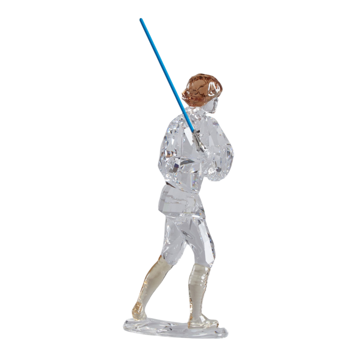 A clear faceted Swarovski crystal figurine of Luke Skywalker holding a blue sword, standing on a transparent base against a plain white background.