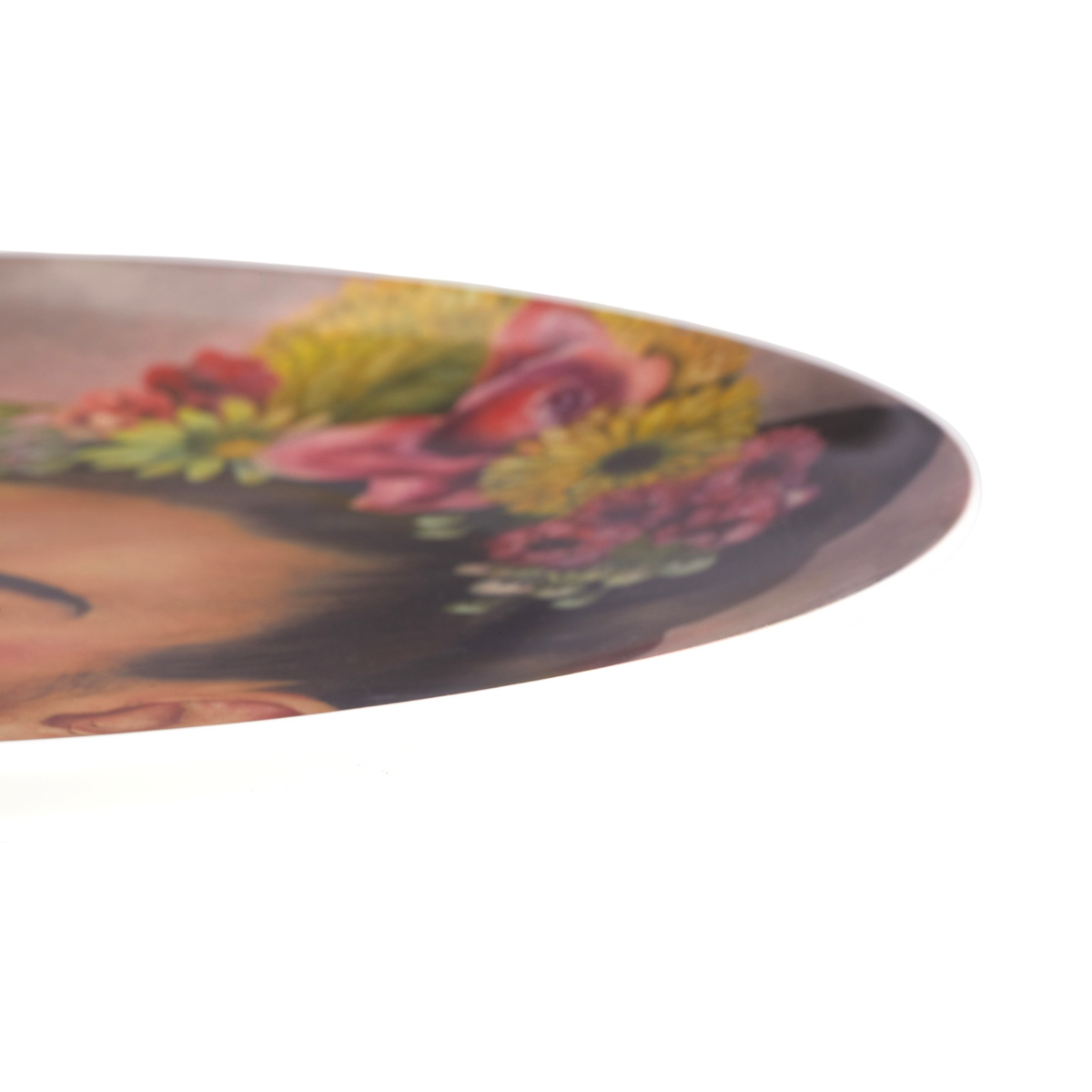 A close-up of a round decorative plate featuring a printed portrait of Frida Kahlo with colorful flowers in her hair, shown against a plain white background.