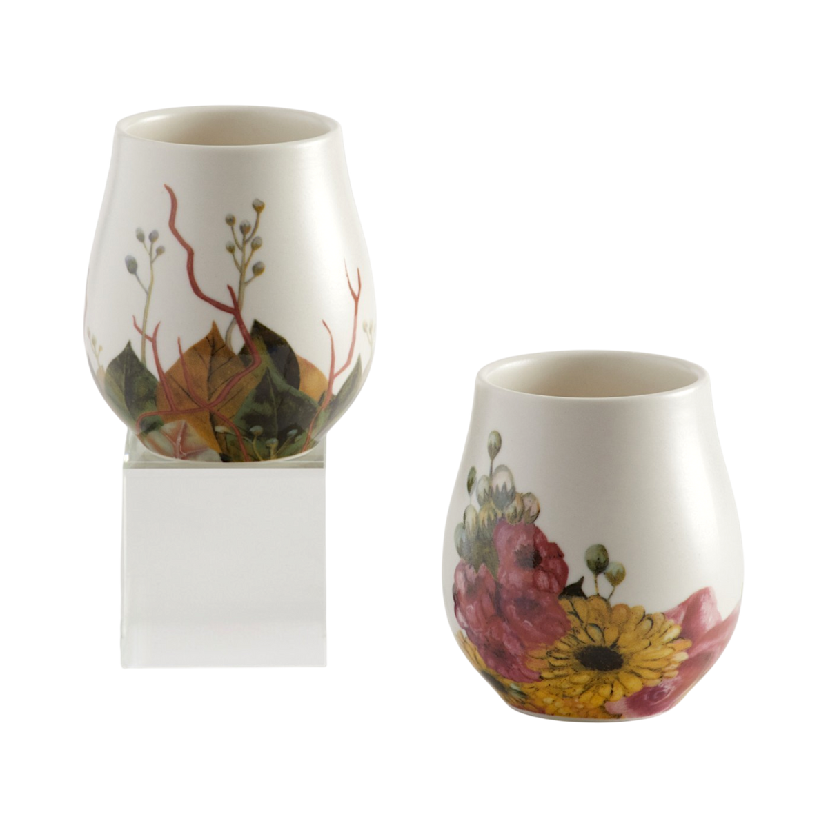 Two small white mugs with hand-painted botanical designs, one featuring pink and yellow flowers and the other featuring green leaves and red stems, on a plain white background.